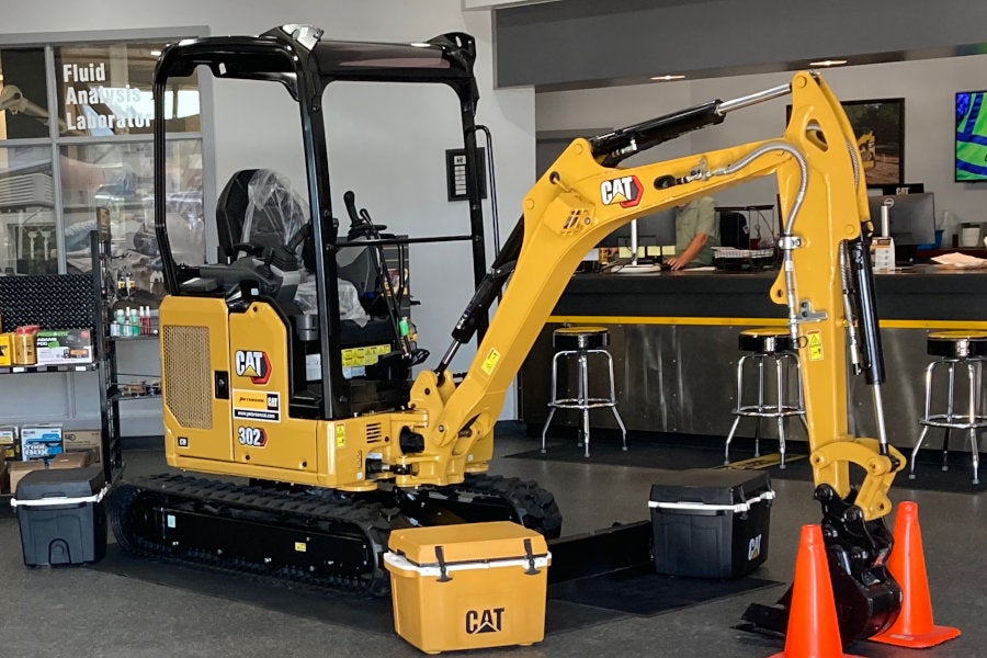 a new Cat 302 mini excavator with a canopy, aux hydraulics, and bucket is polished and on display in the Eugene lobby